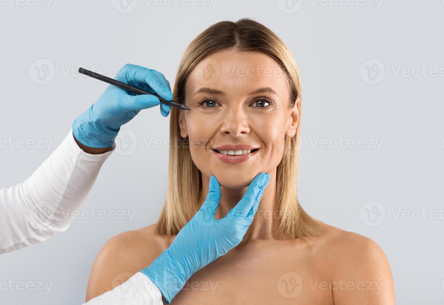 Eyelid surgery, laser blepharoplasty. Beautician hands drawing lines with pen on middle aged woman face, beautiful cheerful blonde lady have plastic surgery at clinic, copy space photo