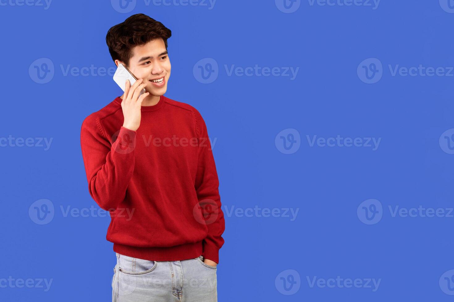 Always In Touch. Portrait of casual smiling asian guy talking on his smartphone, looking aside, standing and posing isolated over blue studio background, banner, copy space. Communication, Phone Call photo