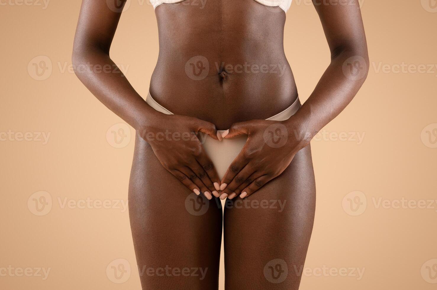Unrecognizable black woman in underwear holding palm in heart-shaped symbol over her panties, posing on beige studio background, cropped, gynecology and womens health concept photo