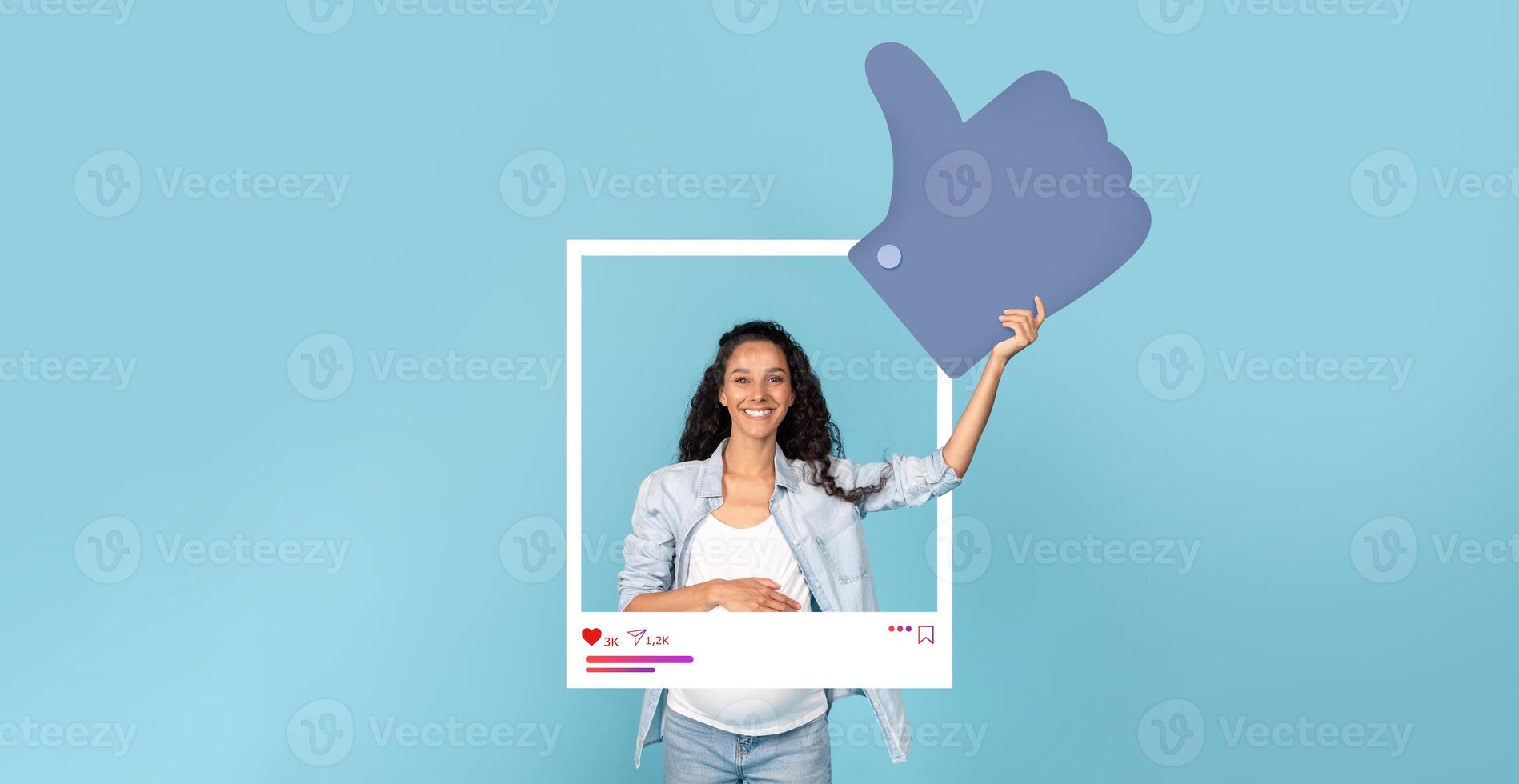 A young woman stands against a bright blue background, smiling as she holds up a large thumbs-up symbol while framed in a social media post outline, representing influencer culture. photo