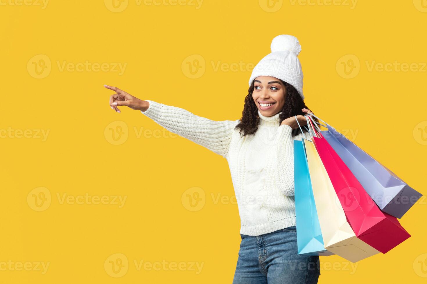 Shopping Offer Concept. Portrait Of Black Woman Pointing Finger Aside At Copy Space For Your Promotion, Carrying Colorful Bags Isolated Over Pastel Orange Background At Studio, Banner, Panorama photo