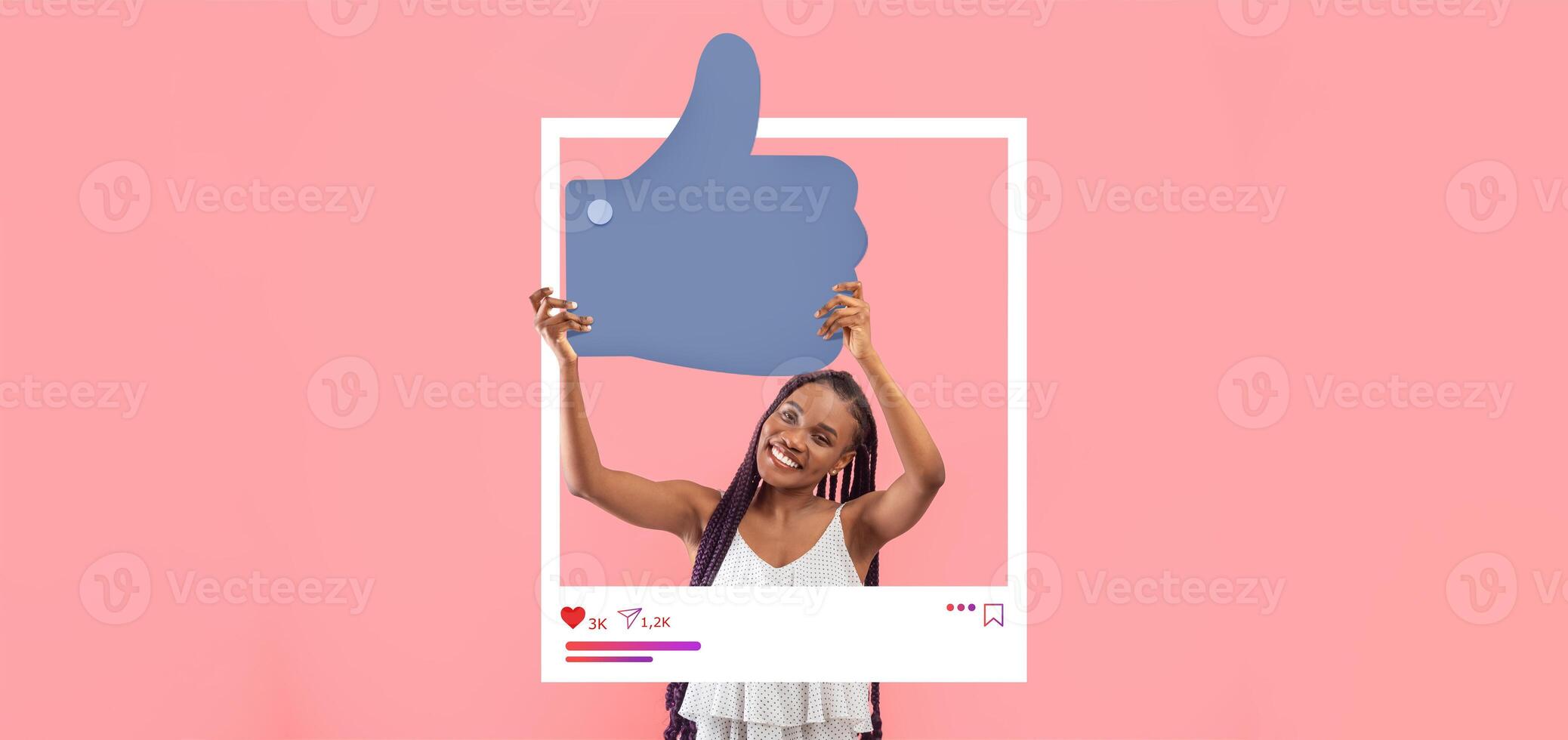 A young woman with long braids joyfully displays a large thumbs-up symbol in front of a pink backdrop. She exudes enthusiasm for her online content and social media presence. photo