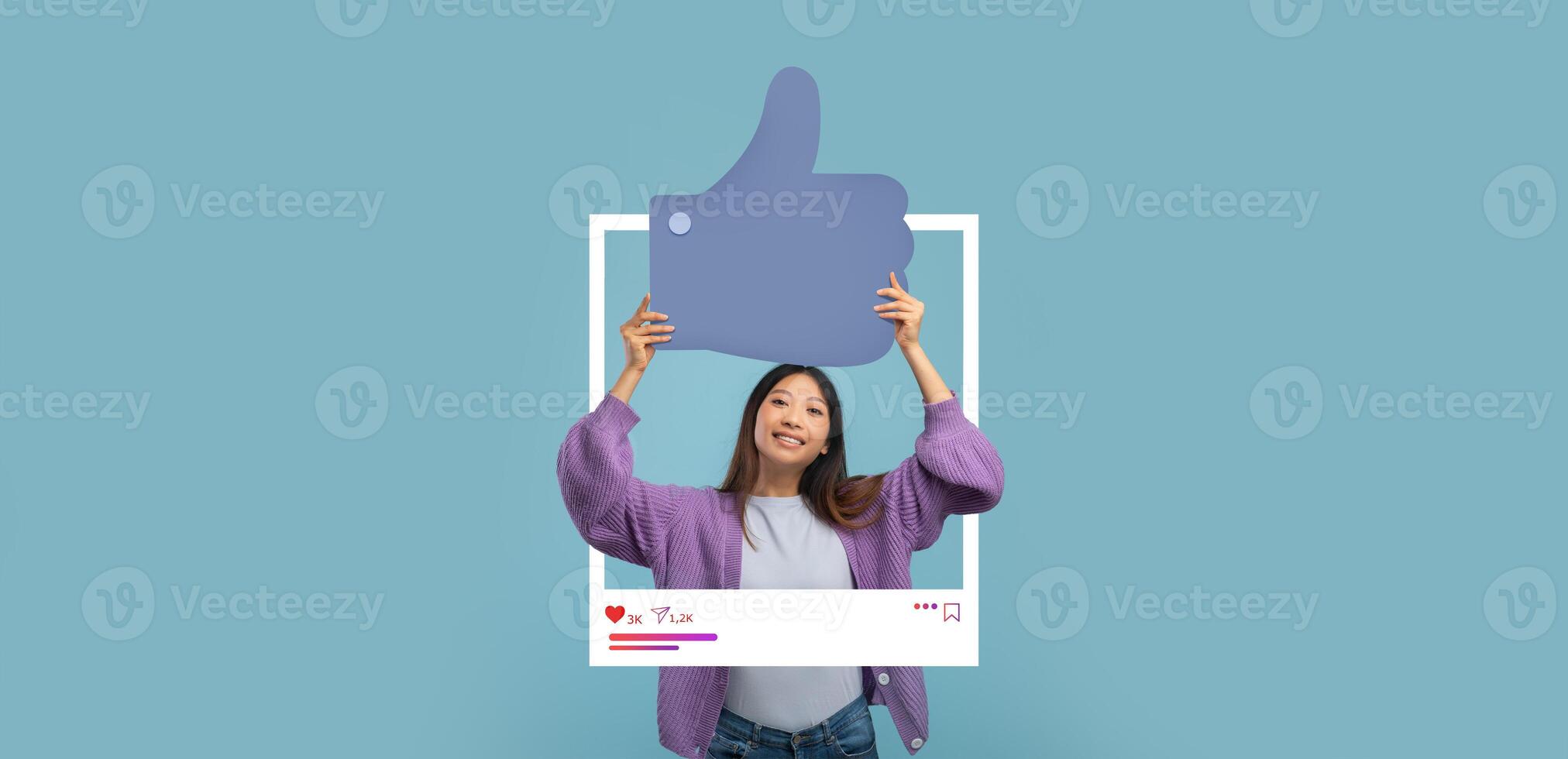 A young woman is joyfully holding a large thumbs up symbol against a light blue backdrop. She represents the positive impact of online engagement for content creators like bloggers and influencers. photo