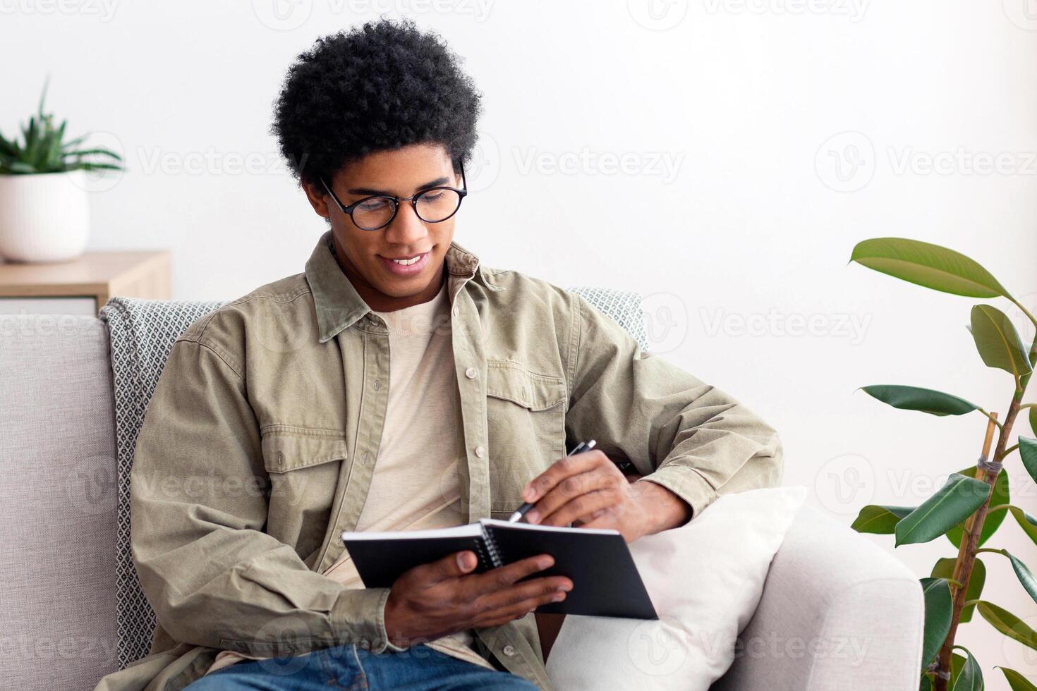 Remote education concept. Black teen college student studying from home during quarantine. African American teenager taking notes for his exam, making homework or getting ready for online class photo