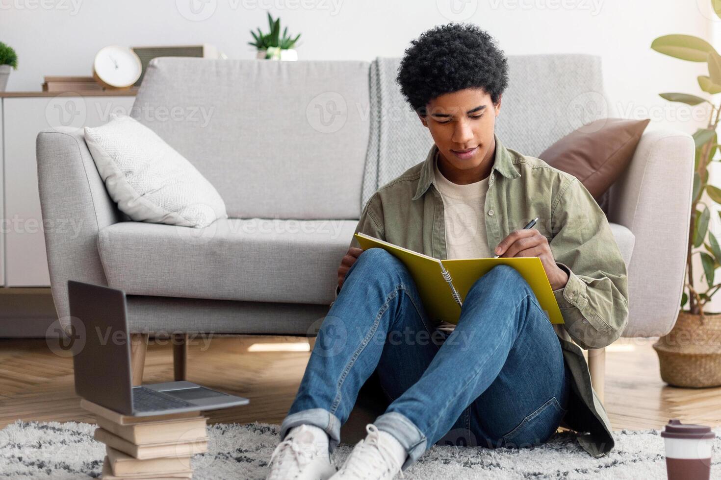 Web based education. Focused black teenager writing down info during online class on laptop at home. Smart African American guy taking notes during web conference or consultation with tutor photo