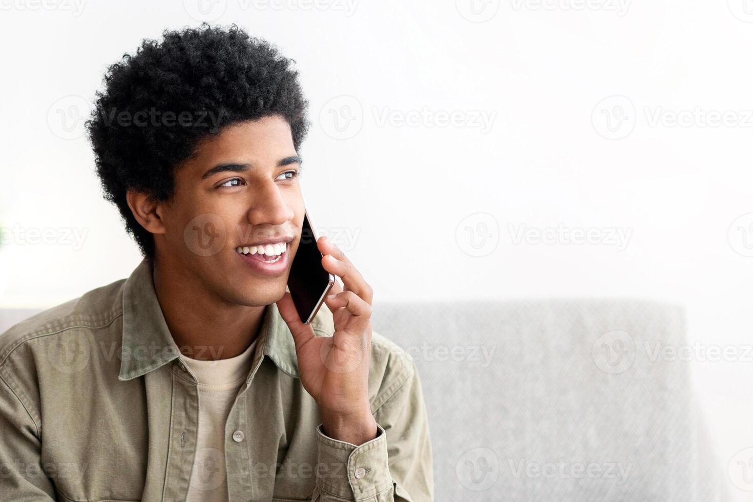 Distance education concept. Happy black student talking on smartphone in front of laptop computer at home. Positive teenage guy participating in web conference, online class or webinar indoors photo