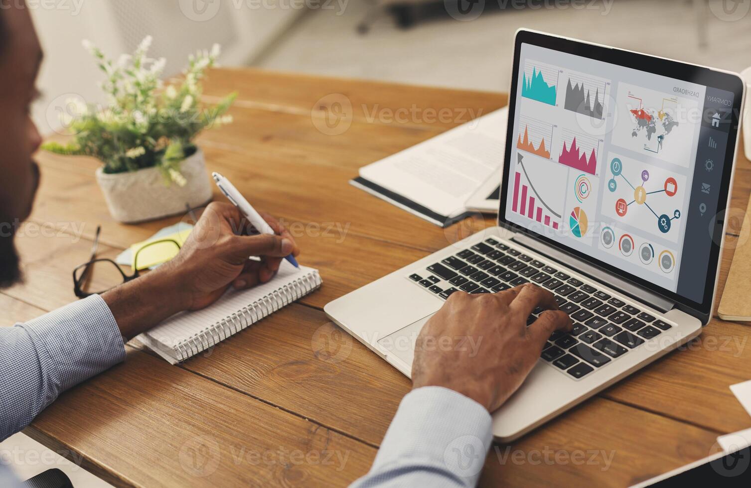 Business Dashboard Concept. Close up back view of black entrepreneur analyzing graph on laptop and writing in notepad photo