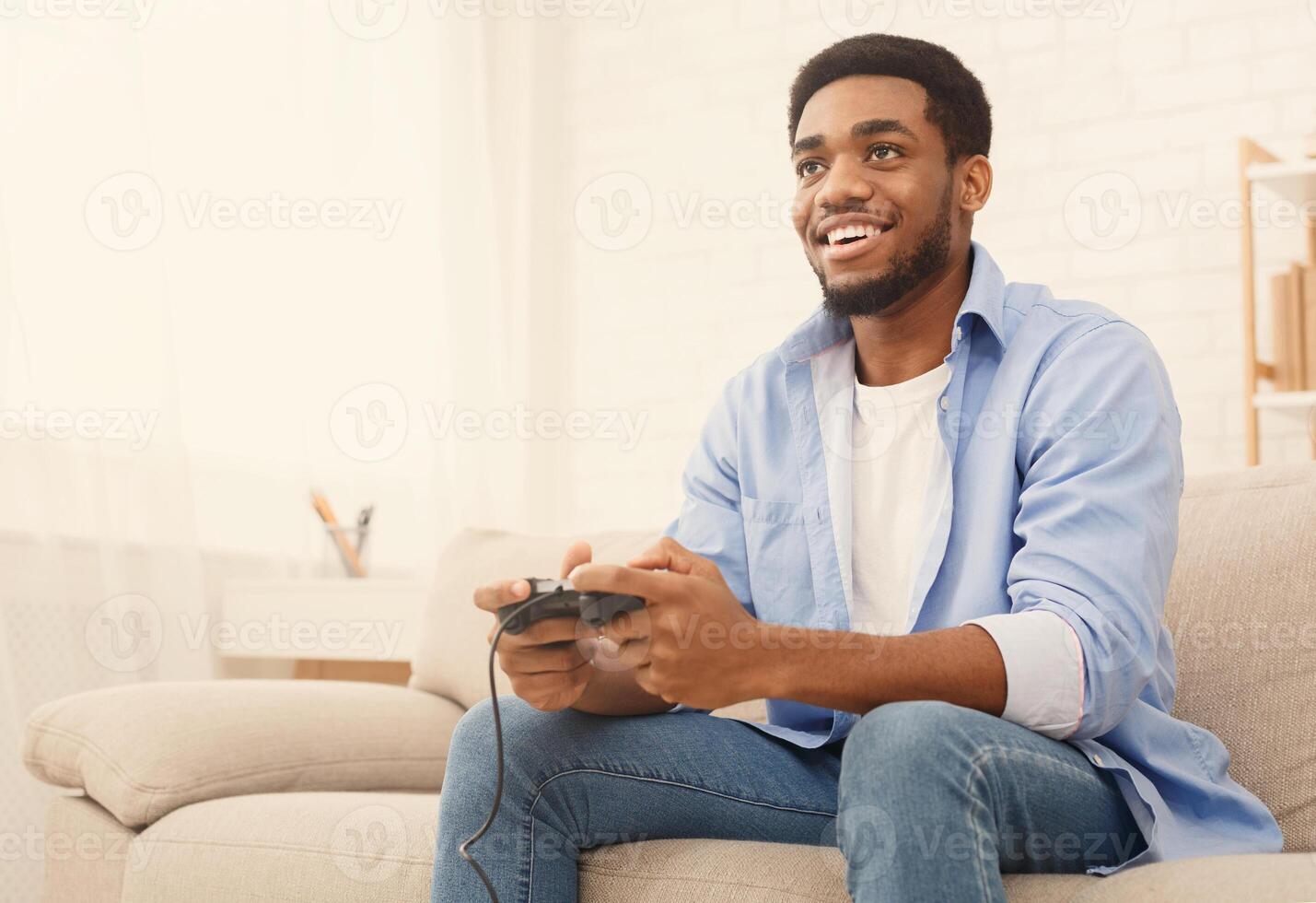 Emotional african-american guy playing game with joystick at home, copy space photo