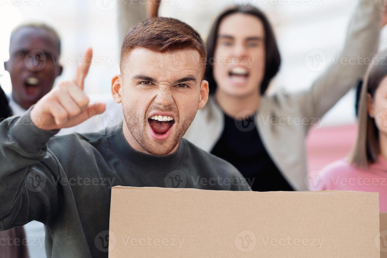 Multiracial demonstrators with empty boards walking by street and chanting slogans against racism. Young caucasian man leading international group of students protesting against government politics photo