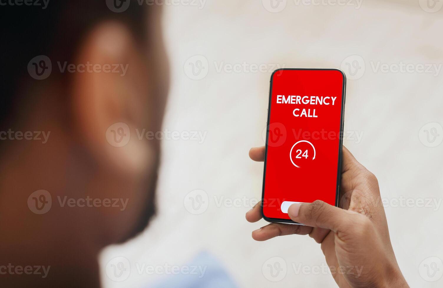 Emergency Call. View over shoulder of man holding phone with 24 hour support line on red screen over blurred background photo