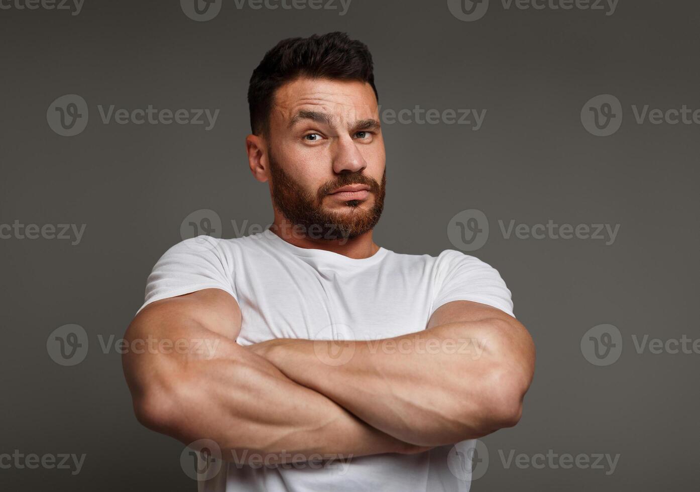 Tough macho with crossed arms looking at camera, gray studio background. photo