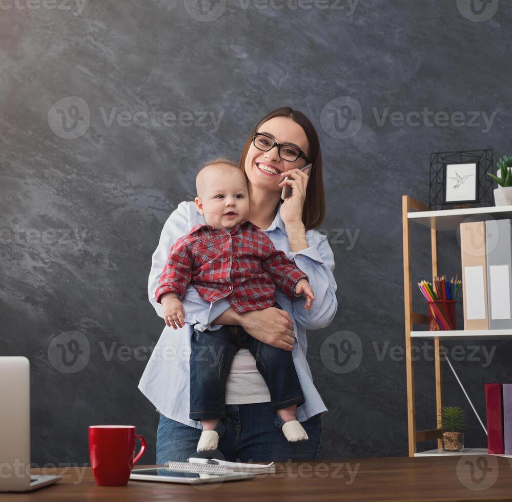 Happy mother working at office with her baby. Young woman talking on phone and using laptop while spending time with her child. Business, motherhood, multitasking and family concept, crop photo