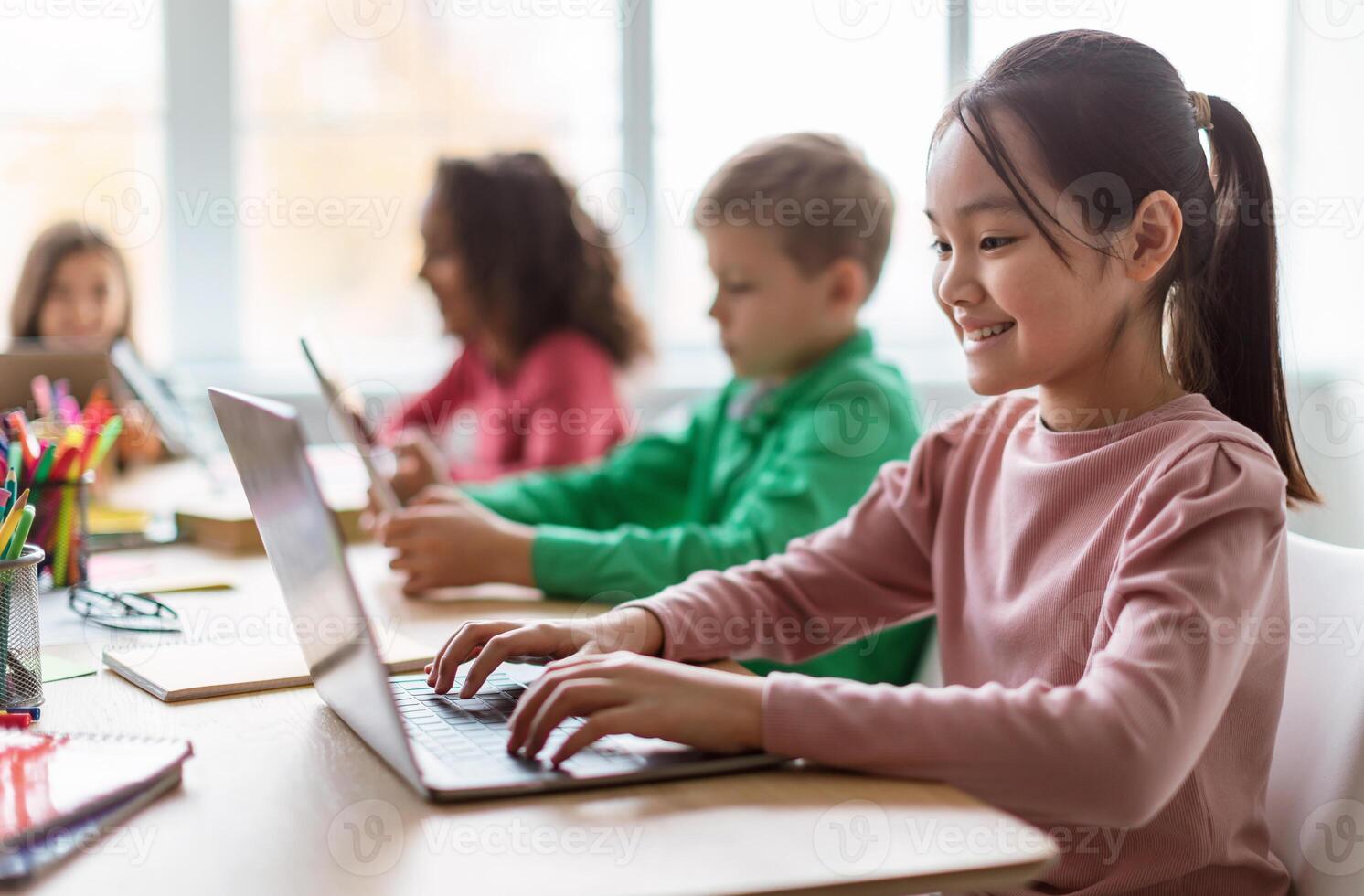 Online Learning. Diverse Children Using Laptop In Modern Classroom At School, Selective Focus On Happy Asian Schoolgirl Browsing Internet On Computer. E-Learning, Education And Technology photo