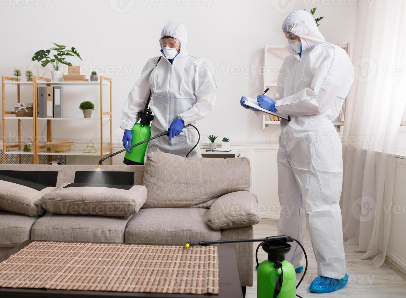 Workers wearing virus protective suits disinfecting home surfaces with spray chemicals to prevent the spreading of the coronavirus photo