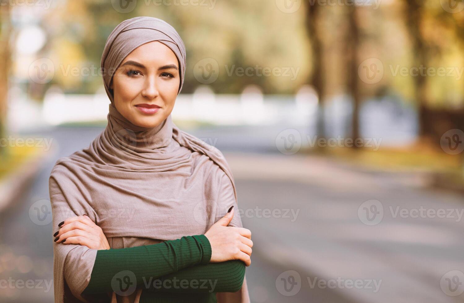 Muslim Woman Wearing Hijab And Modern Clothes Posing Looking At Camera Standing Outdoors In City Park. Portrait Of Modern Islamic Arab Lady. Empty Space For Advertisement Text photo