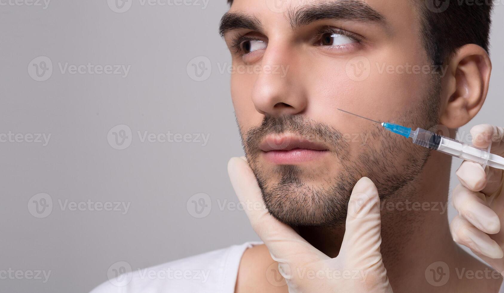 Handsome man receiving filler injection in his face on grey background photo