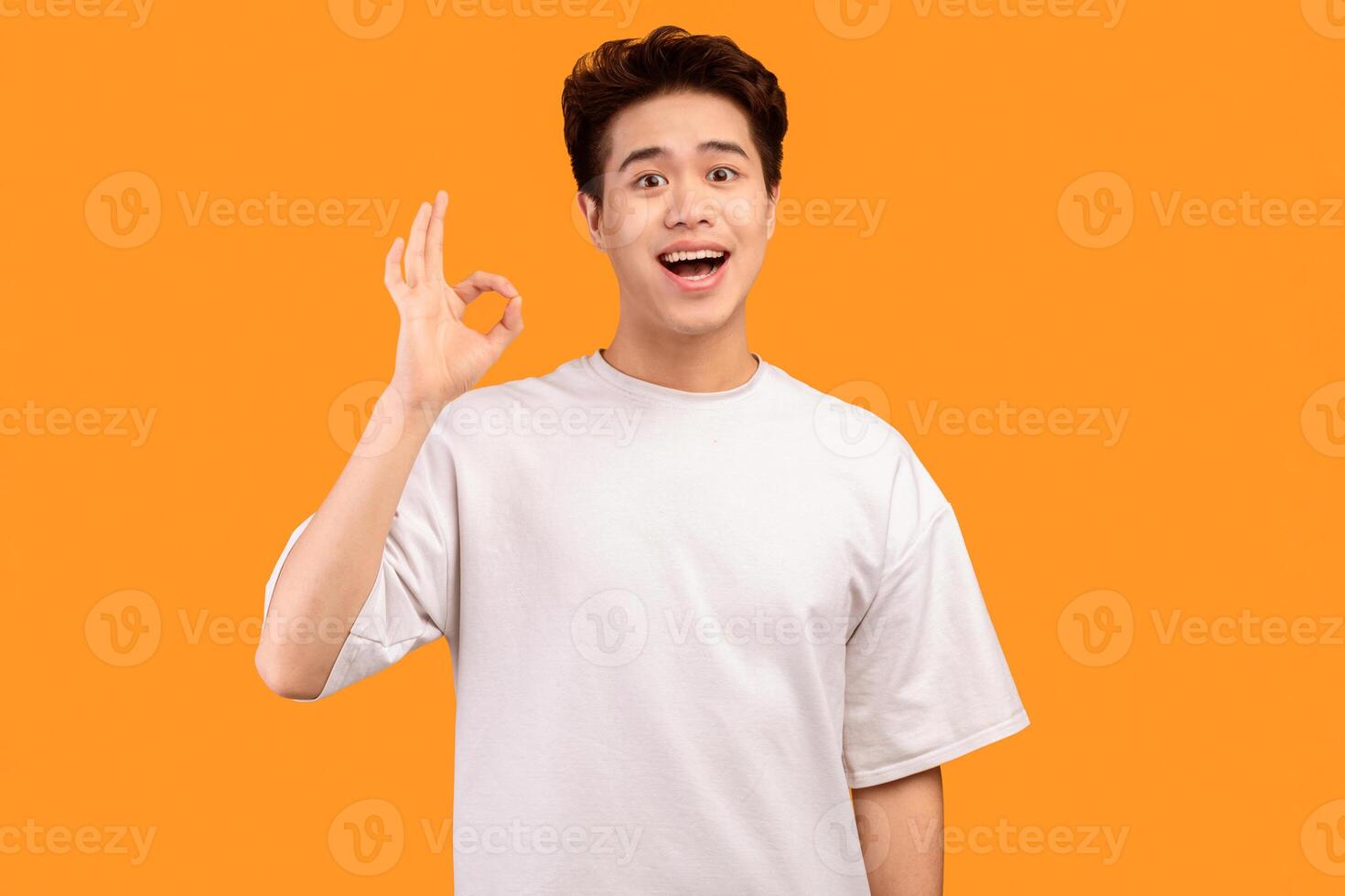 I'm Fine. Portrait of happy excited asian guy doing approval ok gesture with fingers, smiling, showing that he is okay, isolated over orange studio background. Confident positive teen is cool photo