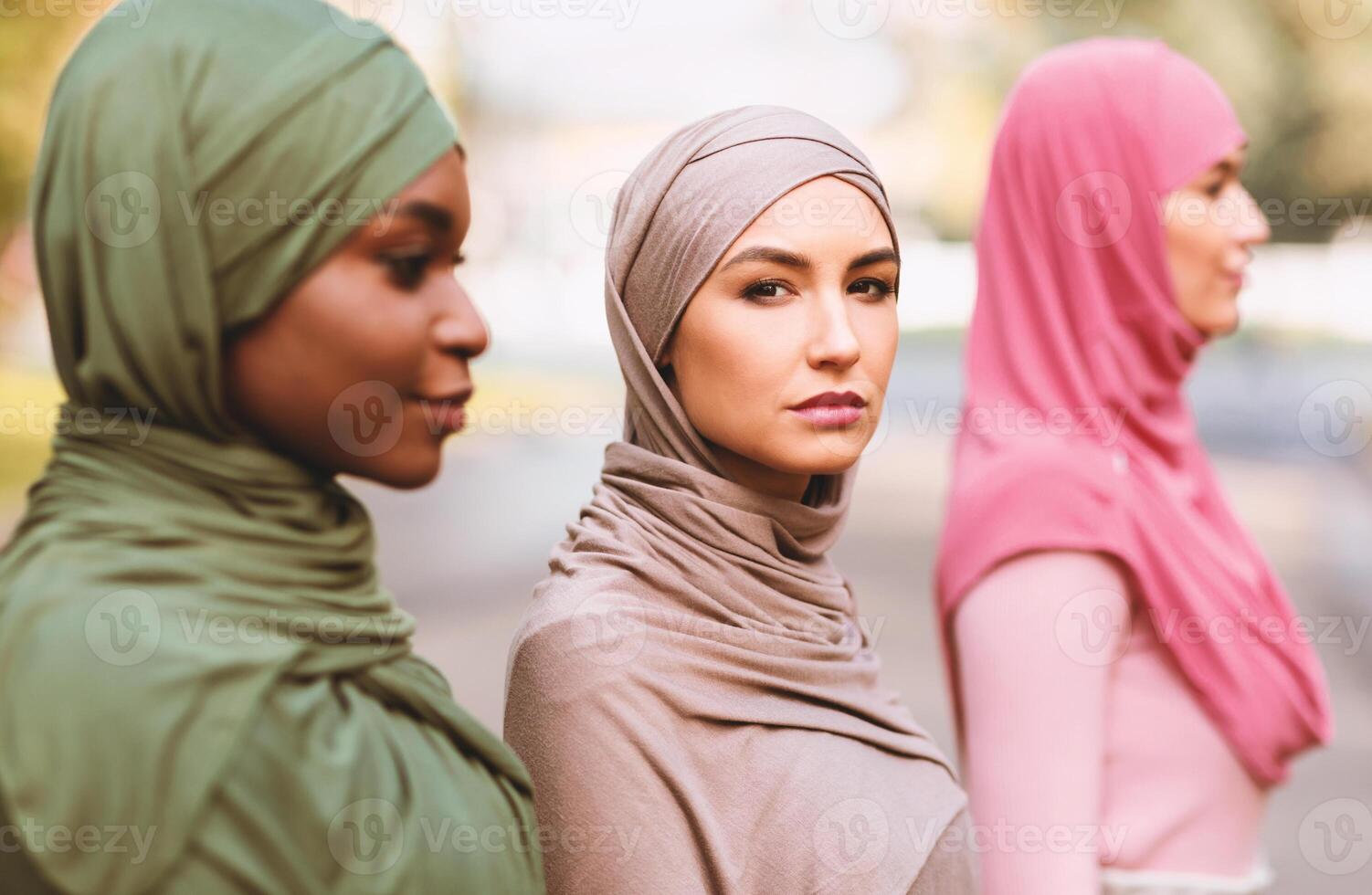 Modern Muslim Females. Group Portrait Of Three Multiracial Islamic Women Wearing Traditional Hijab Headscarf Posing Standing In Line Outside. Selective Focus On Caucasian Arabic Lady photo
