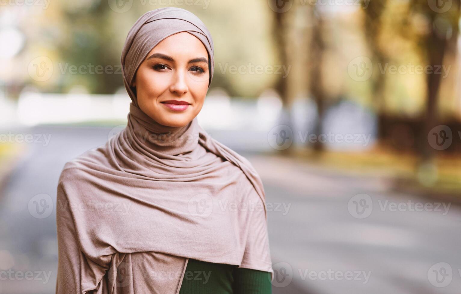 Portrait Of Happy Muslim Woman Wearing Traditional Hijab Smiling To Camera Standing In Park Outdoors. Modern Islamic Arab Lady Posing Outside. Free Space For Your Text photo