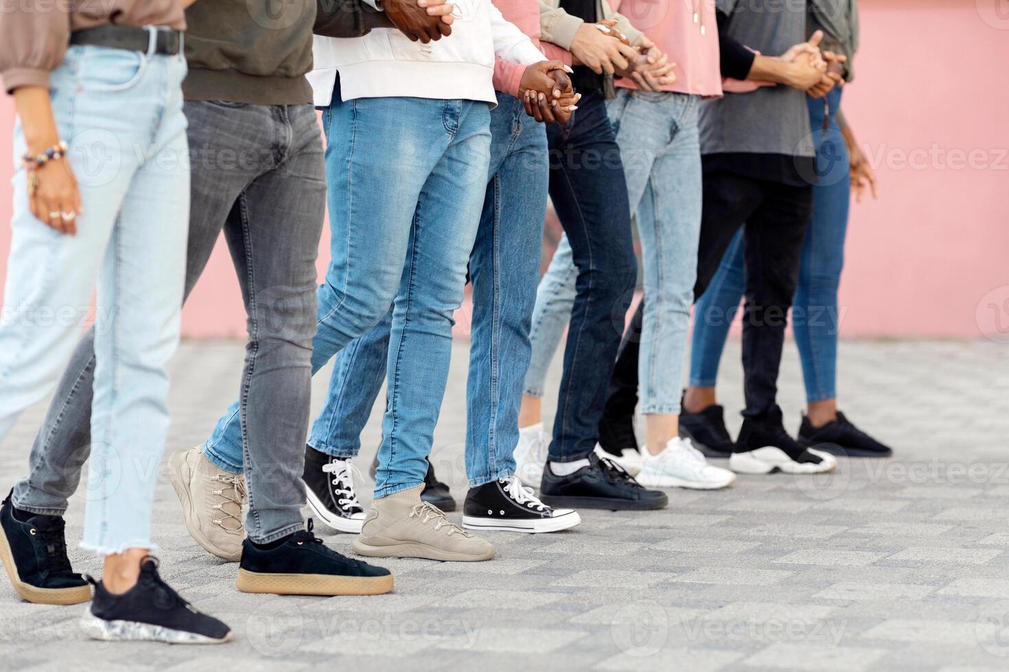 Unrecognizable people holding crossed hands and walking, making strike on the street, side view, panorama. Cropped of multiethnic men and women students activists standing in a row, making live shield photo