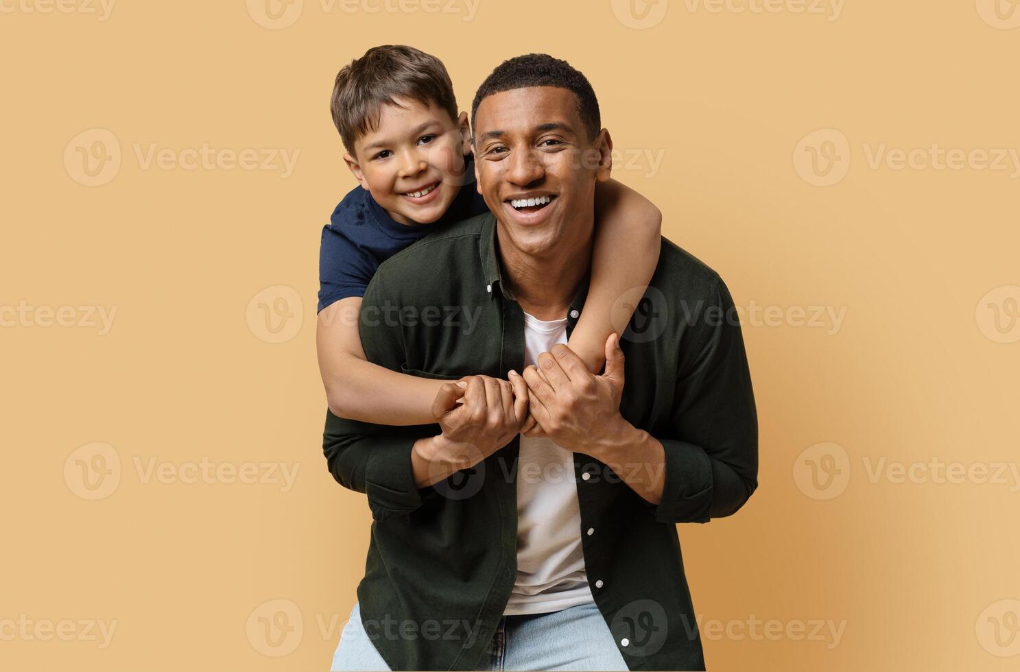 Happy black man have fun posing with cute child preteen boy. Daddy and son embracing and smiling isolated on beige background studio portrait. Fathers Day love family parenthood childhood concept photo
