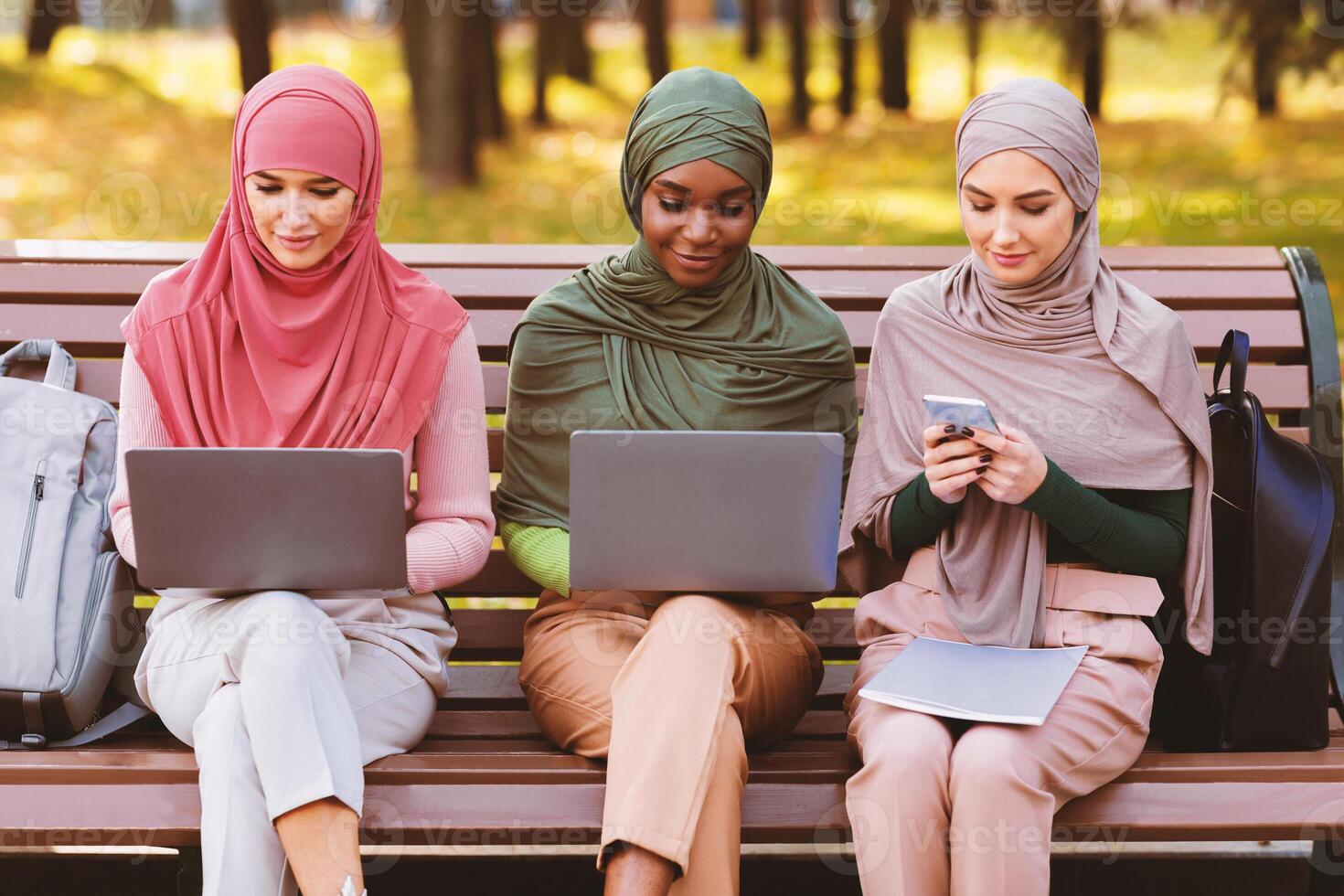 Modern Arab Students Ladies Using Smartphone And Laptop Computers Learning Online Sitting Together In Park Outdoor. E-Learning, Distant Education Concept photo