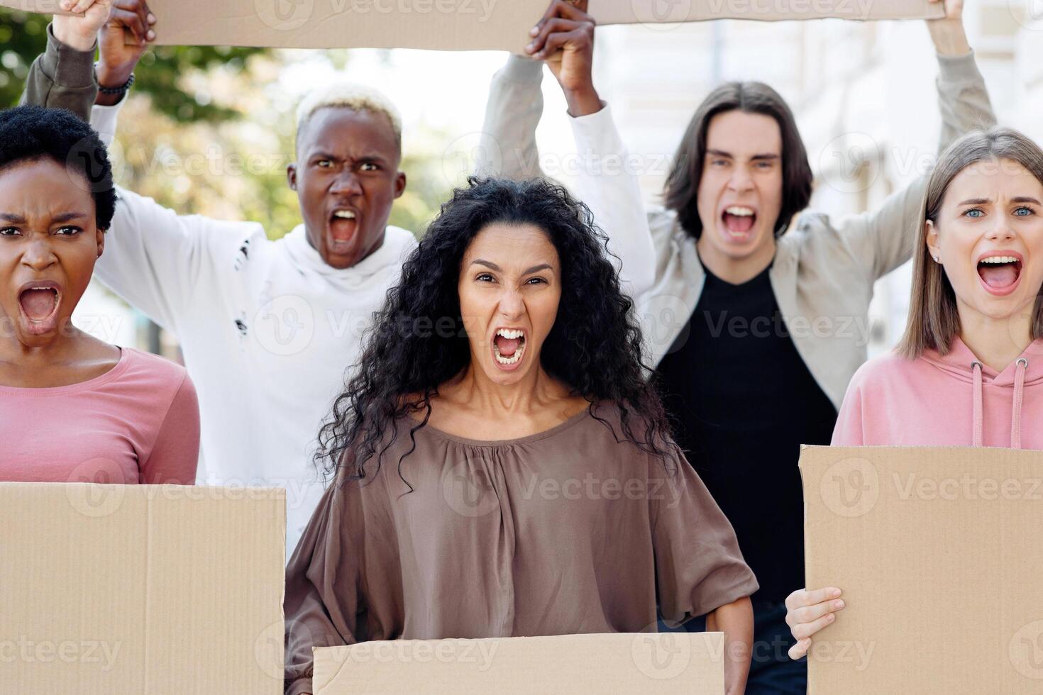 Closeup of desperate strikers with empty placards protesting on the street. International group of young men and women fighting against racism, yelling slogans for human rights photo
