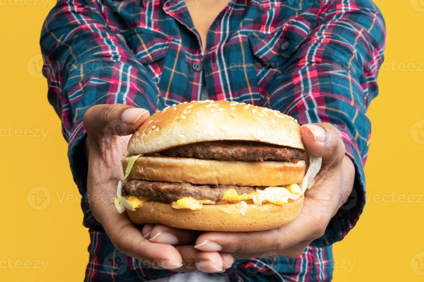 Enjoy Your Meal. Portrait Of Smiling African American Woman Holding Big Tasty Burger, Showing And Giving It To Camera. Black Lady Offering You Fast Food, Isolated Over Orange Studio Background, Banner photo