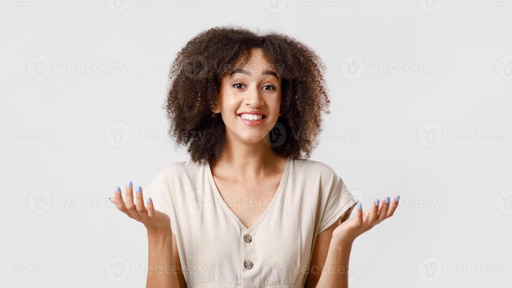 I do not know, can not choose or proposal. Millennial confused african american female student with curly hair in casual, smiles and spreads arms to sides, isolated on light background, free space photo