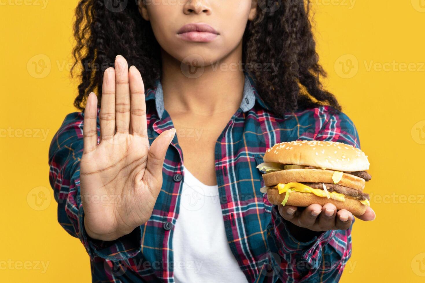 Say No To Fast Food. Closeup Portrait Of Serious African American Woman Holding Burger And Showing Stop Gesture With Palm. Black Lady Rejecting Unhealthy Meal, Isolated Over Orange Background, Banner photo