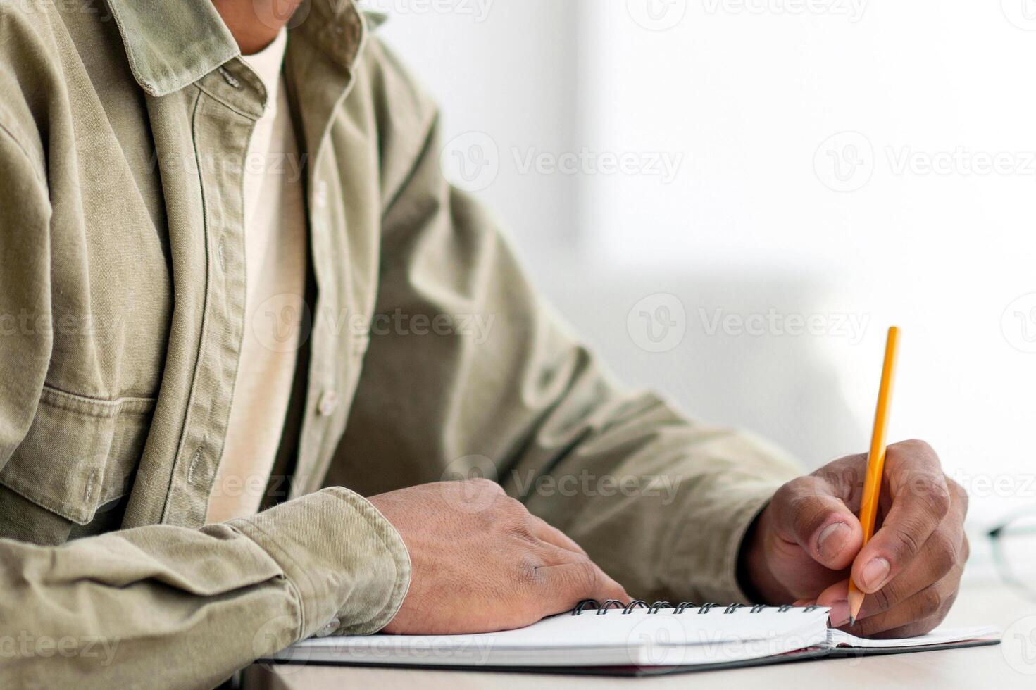 Portrait of positive black teenage student with laptop and notebook looking at camera and smiling at home, copy space. Handsome African American guy studying online, taking notes during web lecture photo