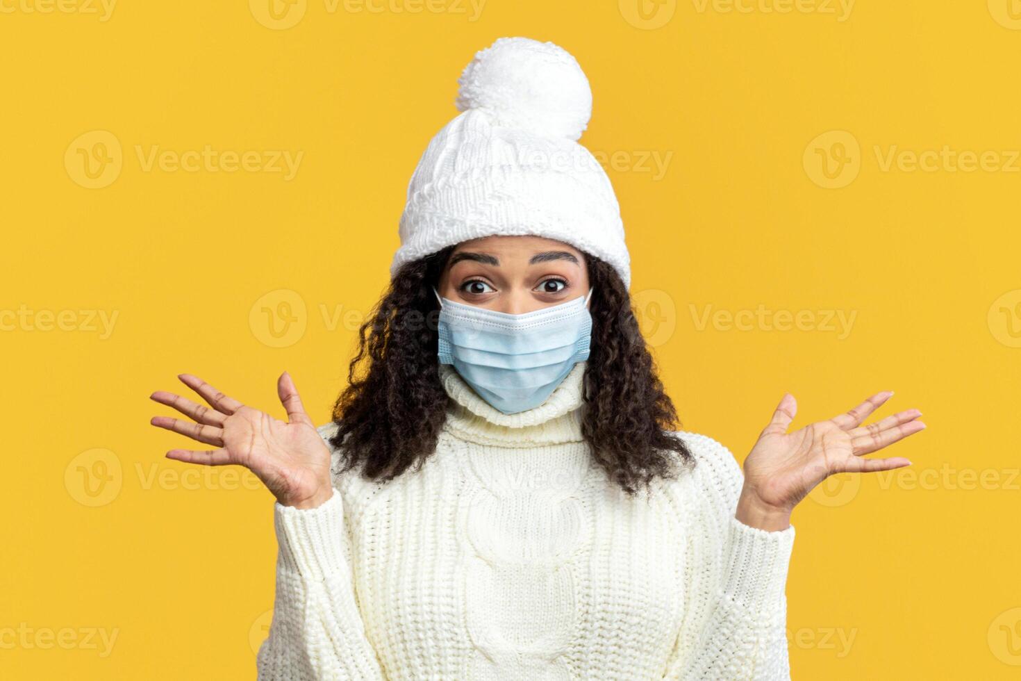 Healthcare and Medicine Concept. Enthusiastic happy black lady in facial mask spreading clean hands, smiling. Positive woman in winter hat supporting social distancing, prepared for going to shopping photo