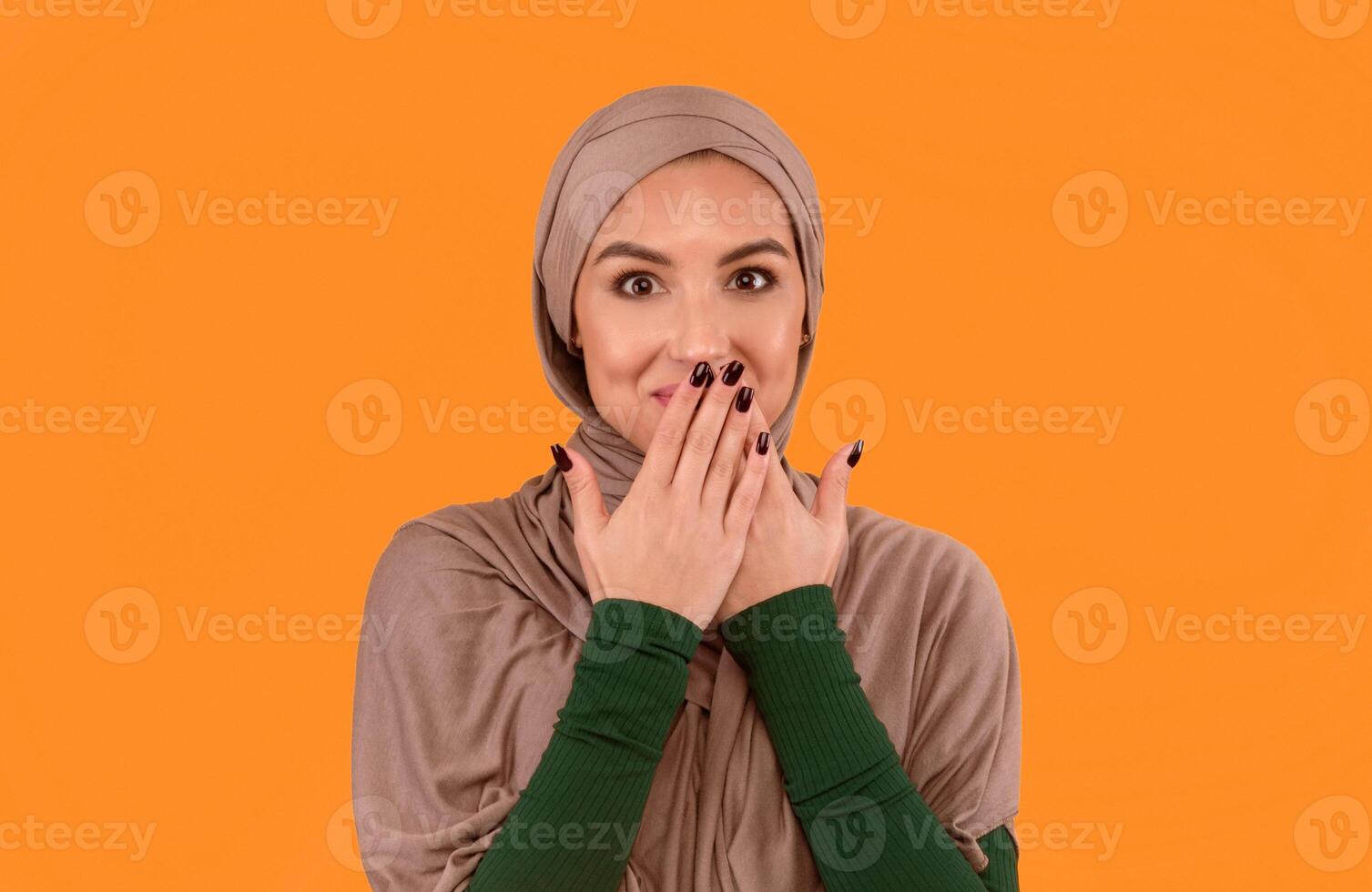 Muslim Lady In Hijab Covering Mouth With Hands Posing Smiling To Camera Standing Over Yellow Studio Background. Rumors Spreading, Oops, Slip Of A Tongue And I Didn't Say It Concept photo