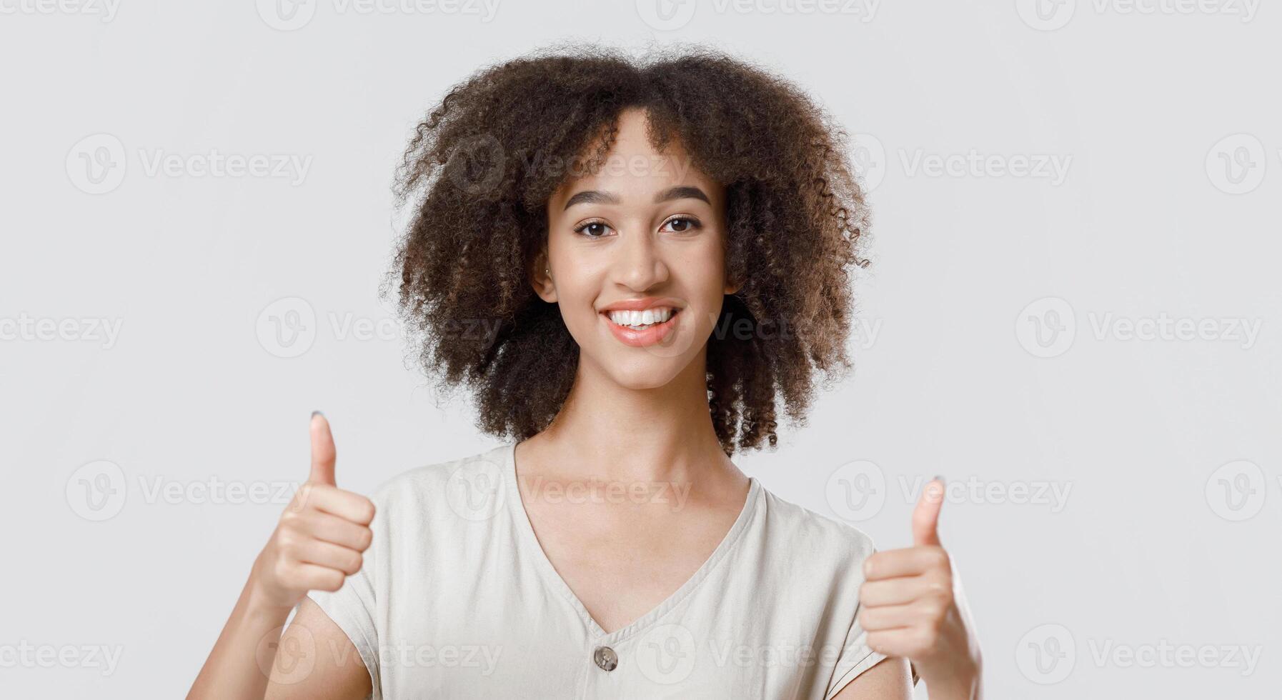 Great result, good choice and cool mood. Happy millennial african american lady student in casual showing thumbs up and looking at camera, isolated on light background, studio shot, free space photo