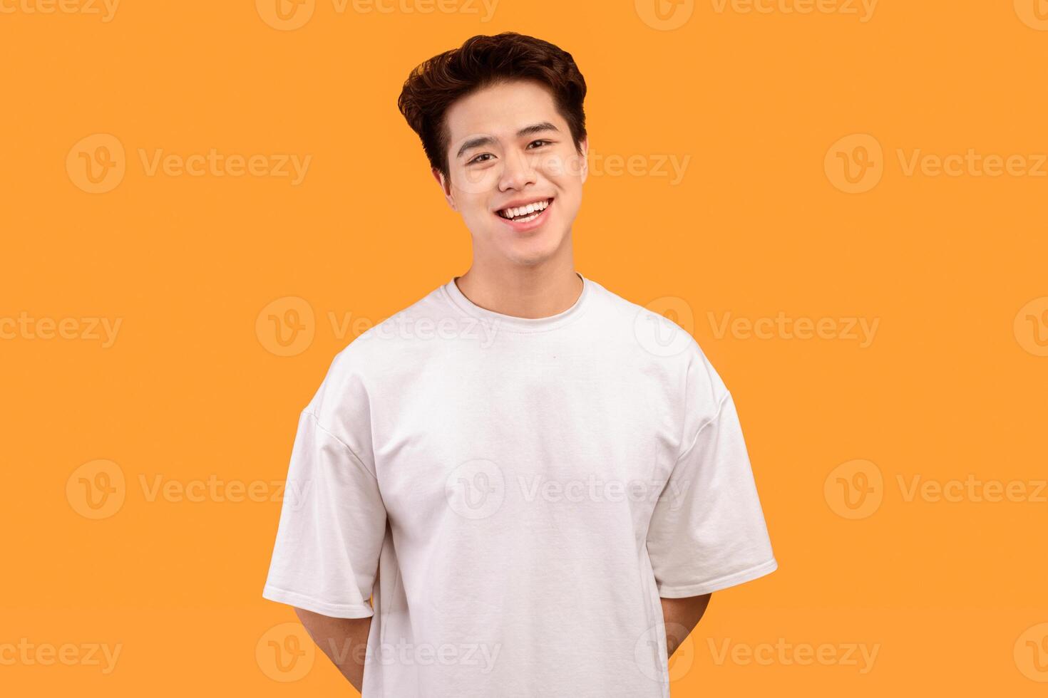 Confident Man. Portrait of smiling asian guy wearing blank white t-shirt for design print mockup, standing isolated over yellow studio background. Happy casual male model laughing looking at camera photo