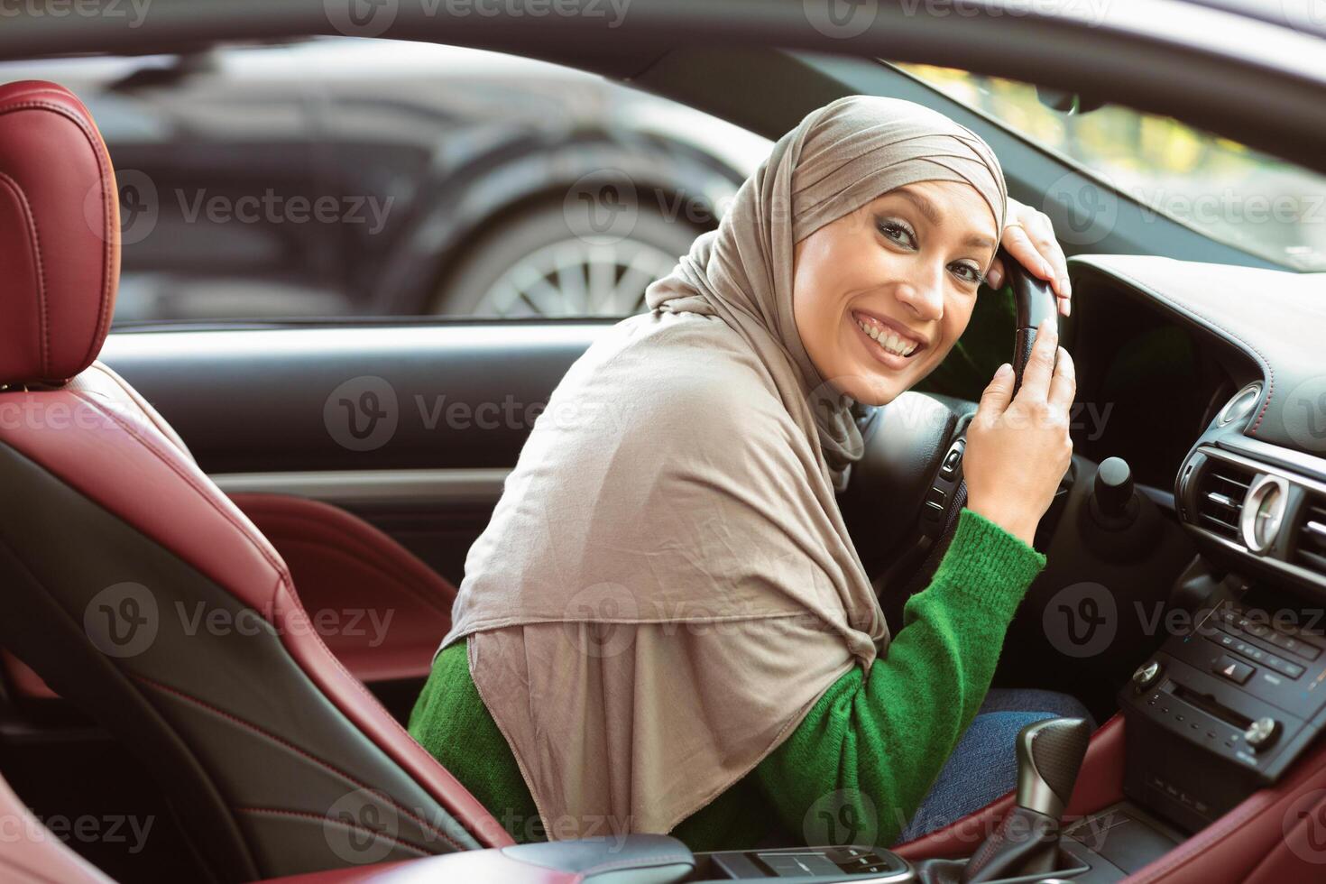 My First Car. Visiting Dealership Showroom. Beautiful muslim woman in headscarf is hugging steering wheel sitting inside her new vehicle and smiling. Young and cheerful lady enjoying purchase photo