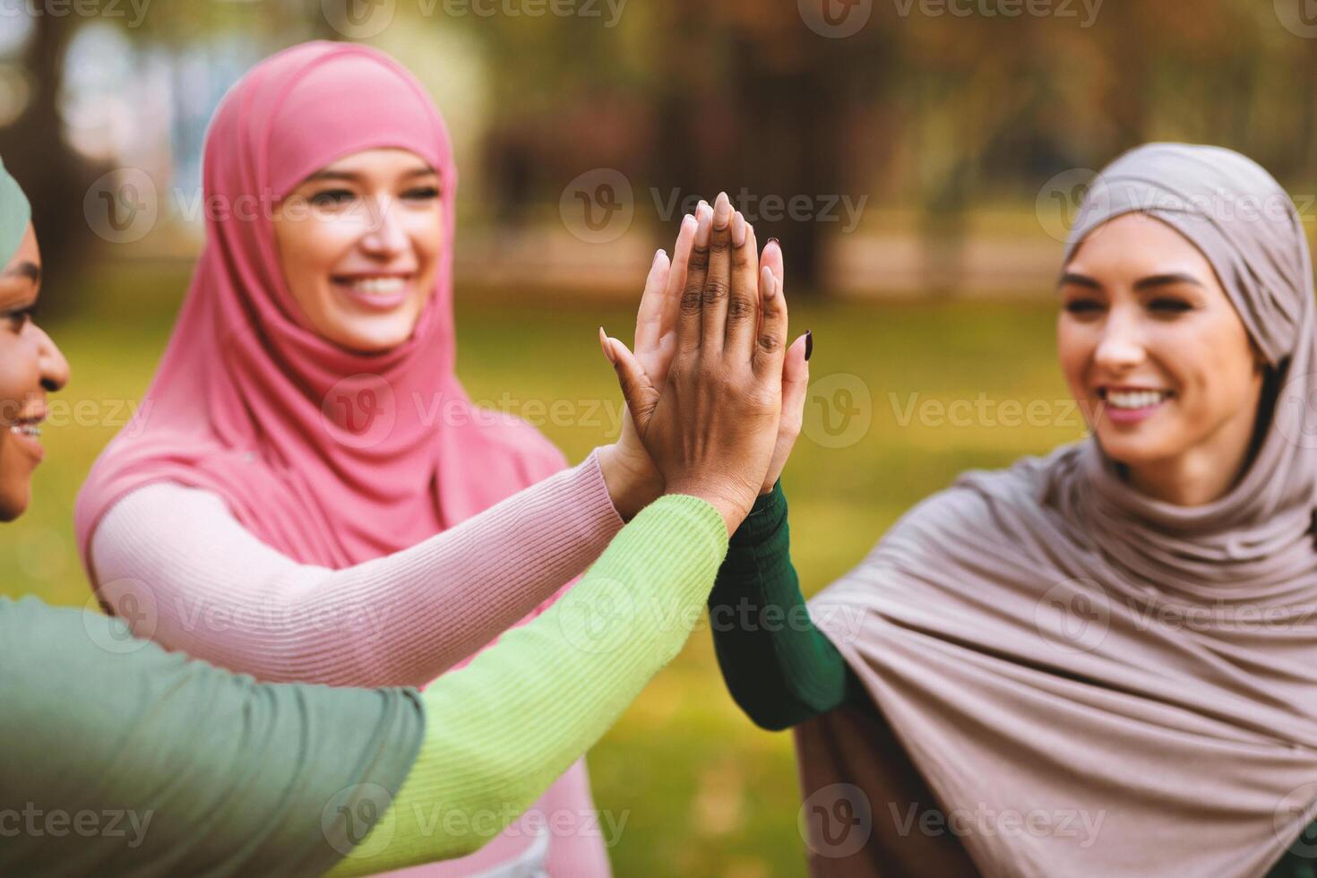 Three Happy Modern Muslim Ladies In Hijab Giving High Five Standing In Park Outside. Arabic Women Unity And Togetherness, Female Friendship Concept. Selective Focus On Hands photo