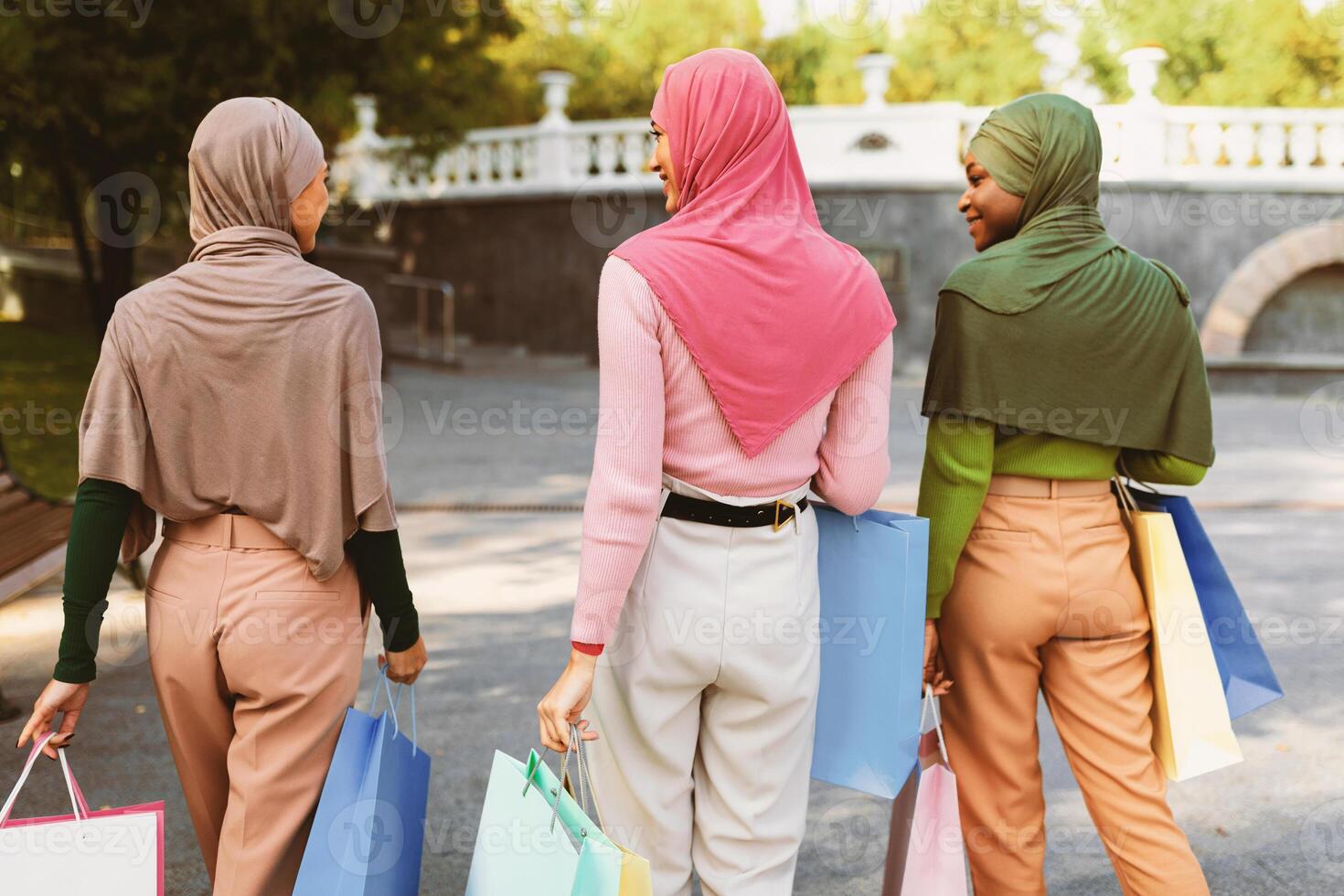 Three Muslim Women Walking With Shopper Bags After Successful Shopping Outdoors. Back View Of Unrecognizable Diverse Islamic Females In City Park. Fashion And Style Concept. photo
