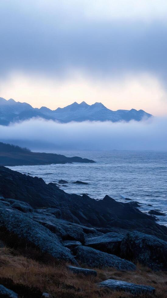 Misty Mountain Majesty A Serene Coastal Landscape. The tranquil fusion of sea, mountains, and fog creates a breathtaking, dramatic scene. Perfect for nature lovers and those seeking serene beauty. photo
