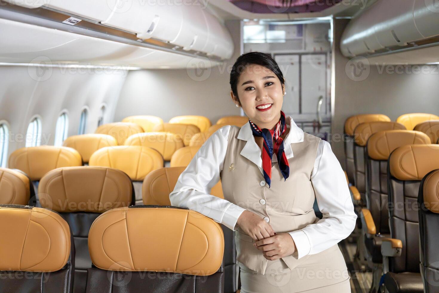 Asian flight attendant posing with smile inside aircraft for welcoming passenger on board with seat on the background for airline travel usage photo