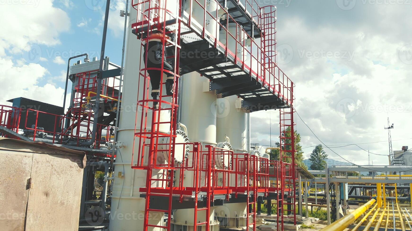 Aerial view gas station operator descends from the top of the station. Modern gas complex in the mountains. A gas worker climbs the ladder of the gas distribution unit, photo