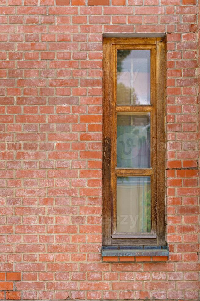 Narrow stylish window in a wooden frame in a red brick wall. Fragment of a residential building. photo