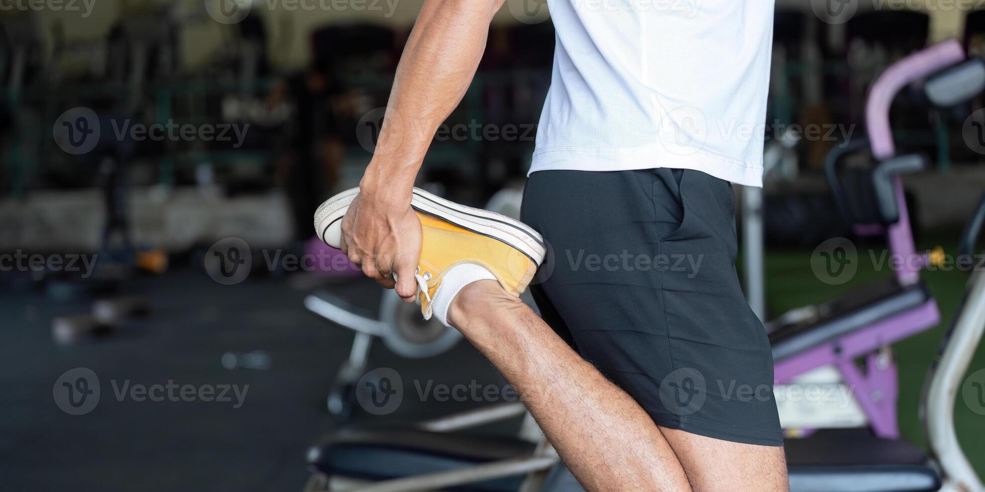 Wellness and Fitness. Young man stretching leg in gym for better flexibility and health. photo