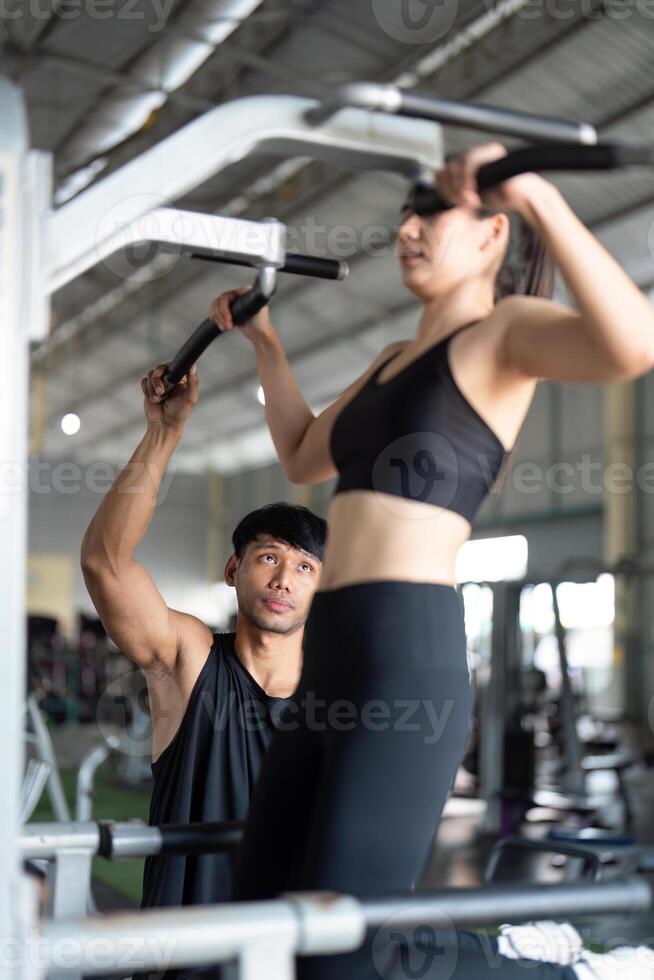 Wellness and Fitness Coaching. Personal trainer guiding woman on pull-up machine. photo