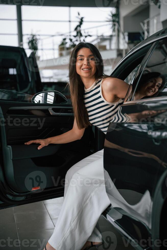 Going ,,out the door. Beautiful young woman is with new automobile in car showroom photo