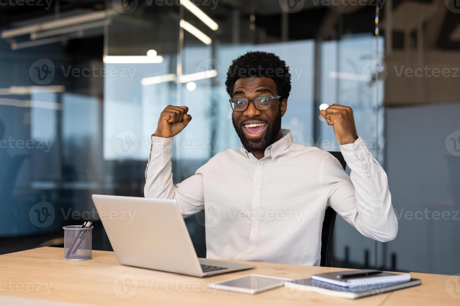 An ecstatic businessman celebrates a win, showing excitement while working on a laptop in the office. photo