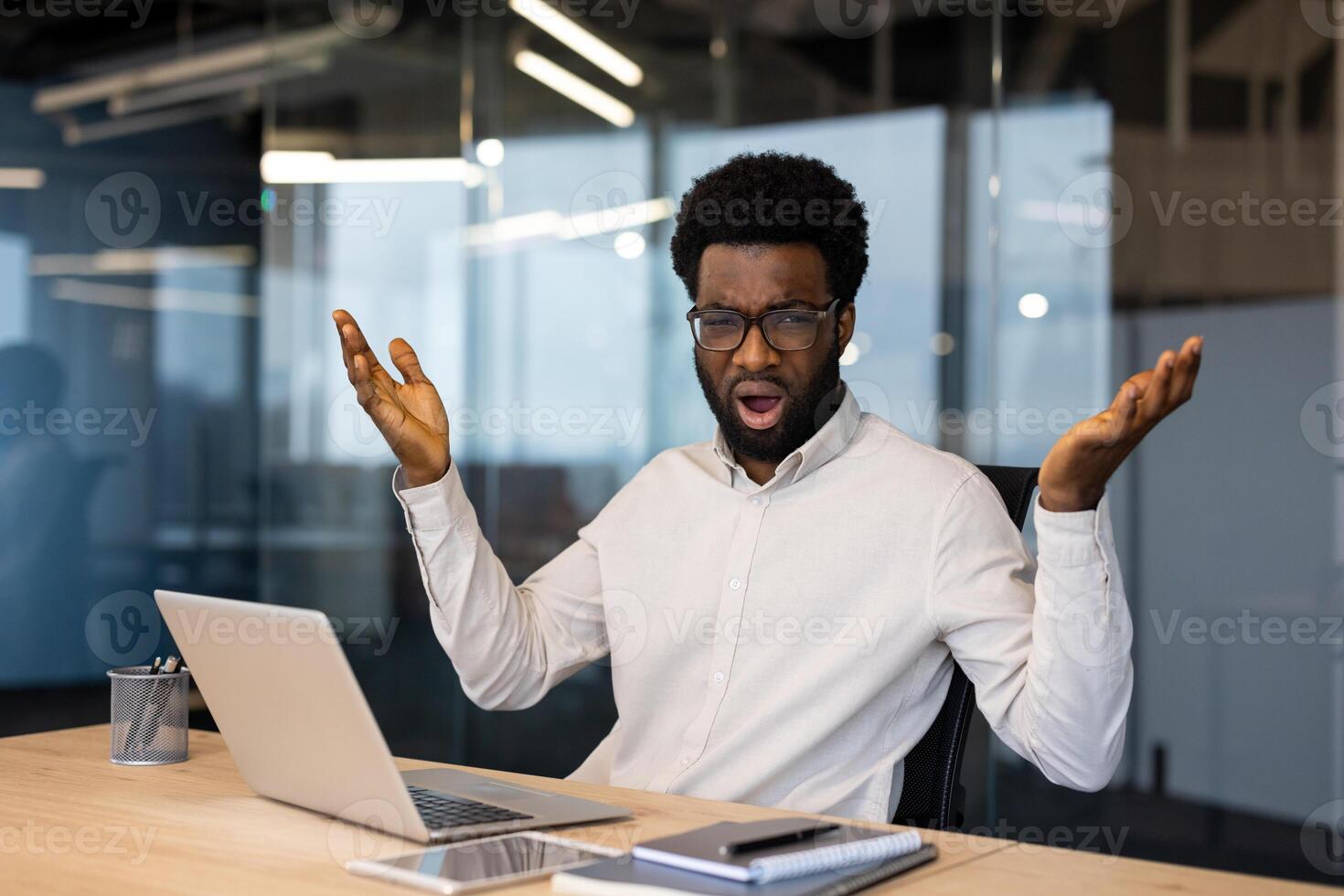 Portrait of upset and disappointed man inside office. Businessman looking nervously at camera while working with laptop at workplace. photo