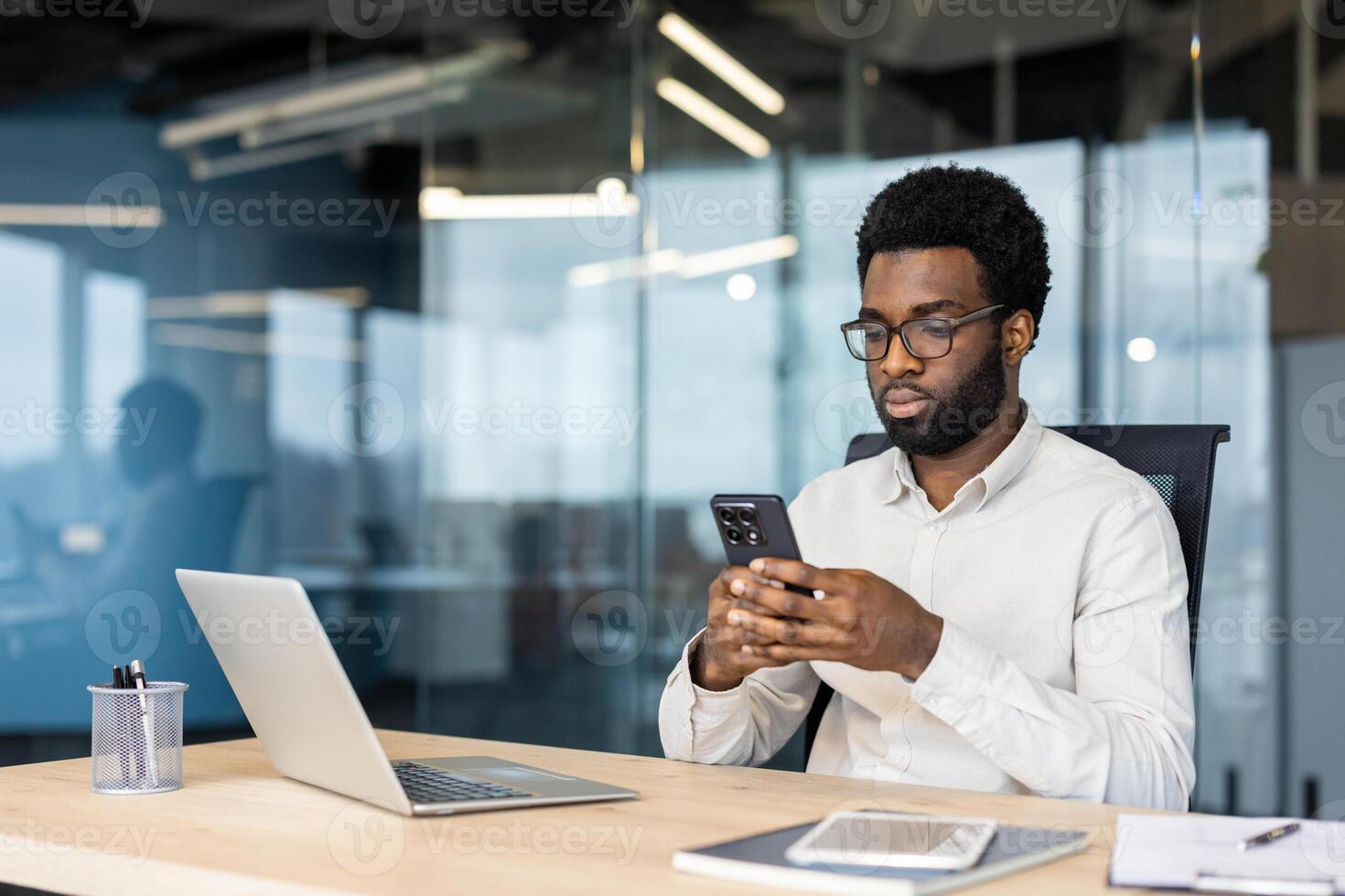 Serious focused man using app on phone. Businessman thinking sitting at desk in middle of office, typing text message on smartphone, and browsing online internet pages. photo