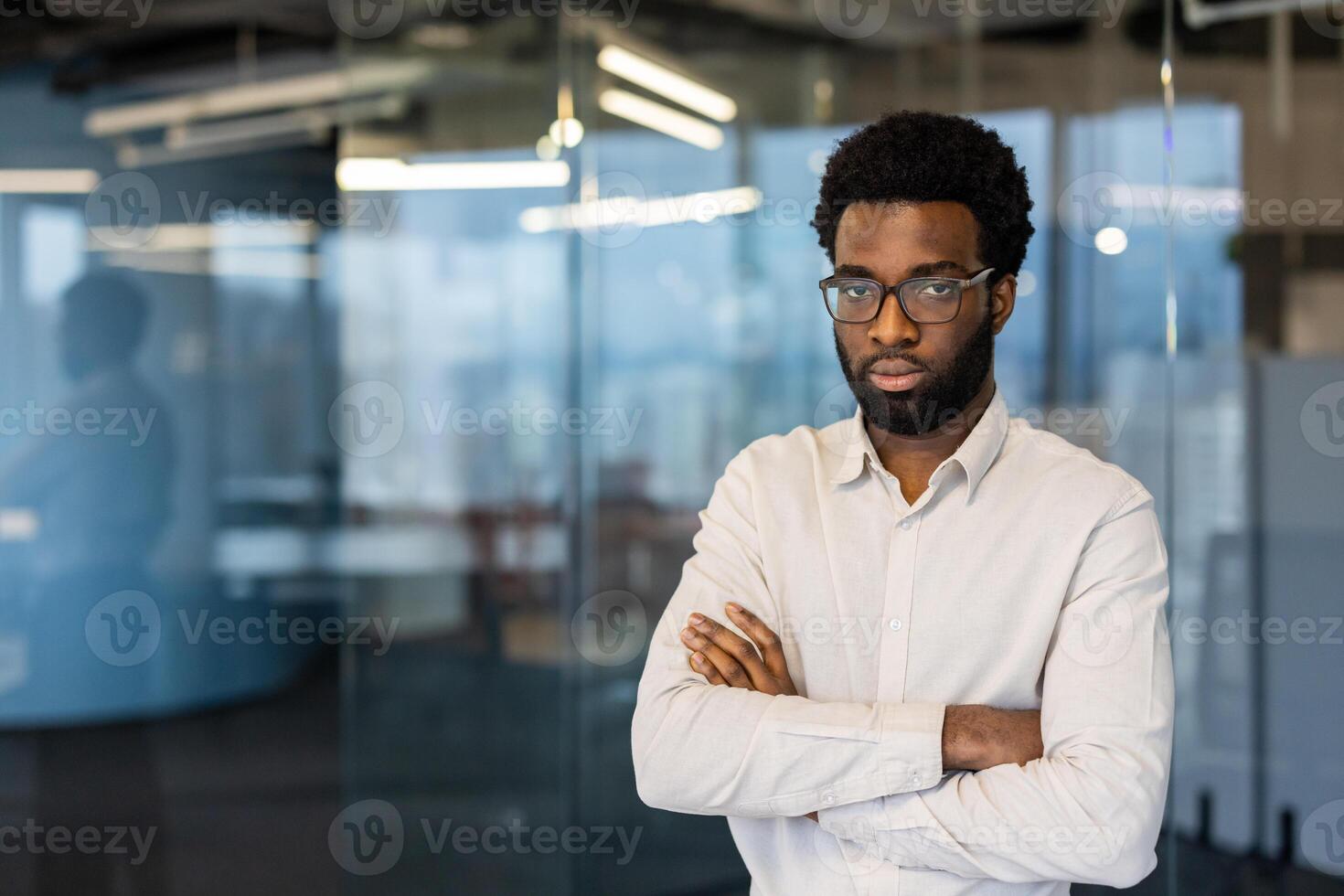 An African American man stands confidently with his arms crossed in a modern office space, exuding professionalism and determination. photo