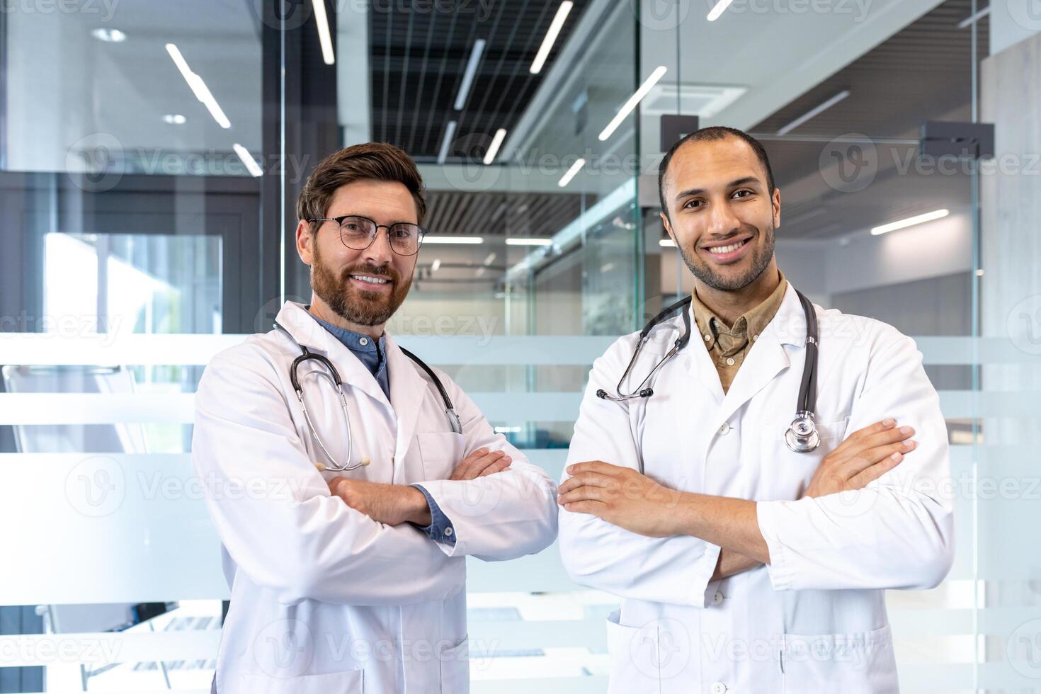Two smiling doctors in white coats and stethoscopes pose confidently with arms crossed, ready for consultation. photo